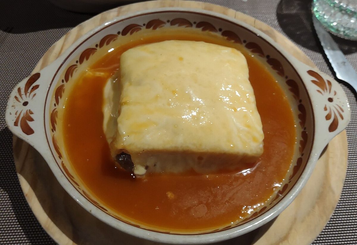 A francesinha under melted cheese and tomato-and-beer sauce in an earthenware dish