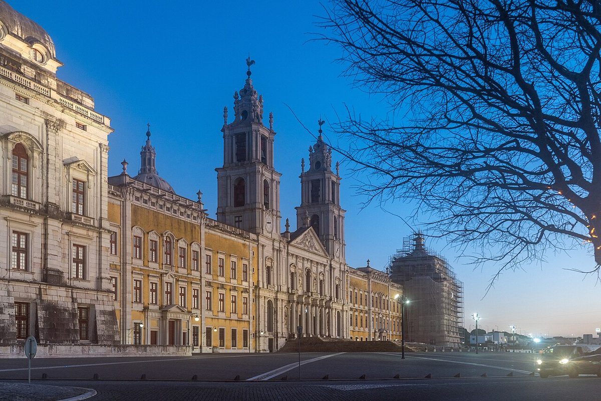 The long west front and twin bell towers of the Mafra National Palace at dusk