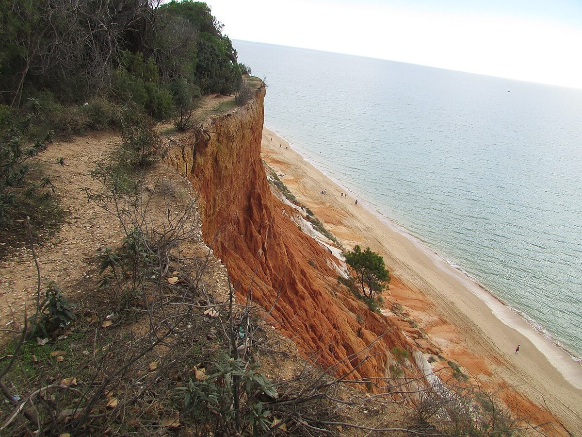 The ochre and rust-coloured cliff wall running above the long sand of Praia da Falesia