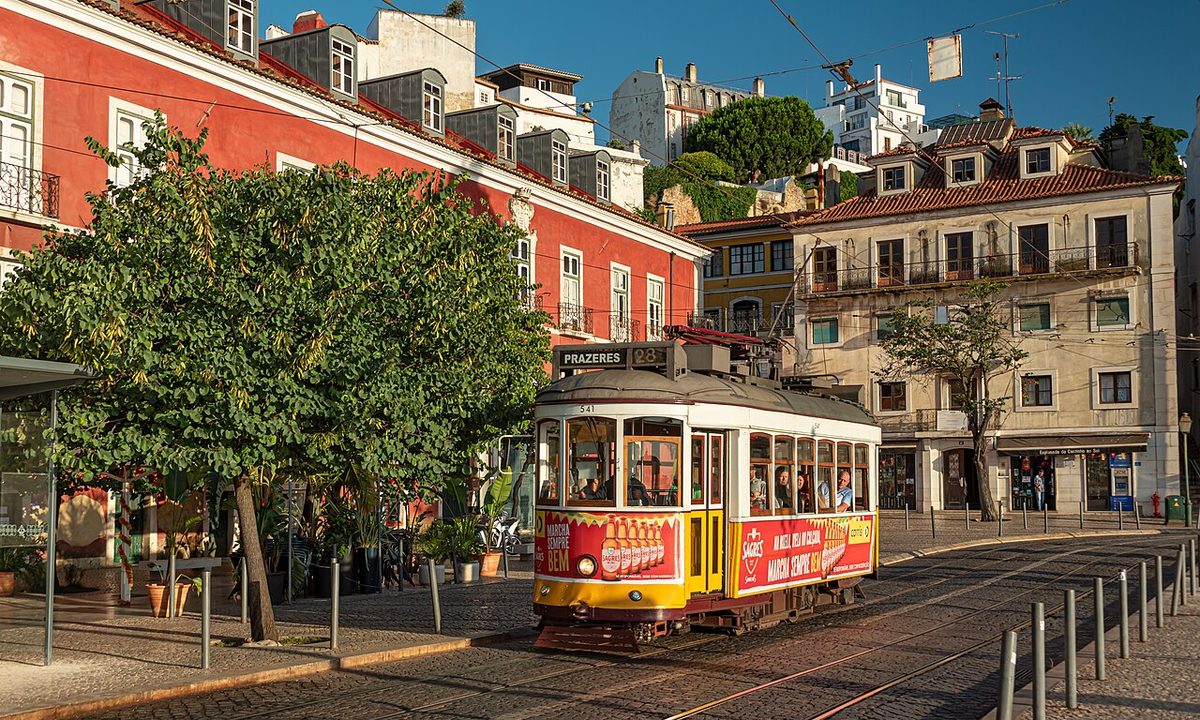 A yellow number 28 tram climbing a narrow street in Alfama, Lisbon, in late afternoon light